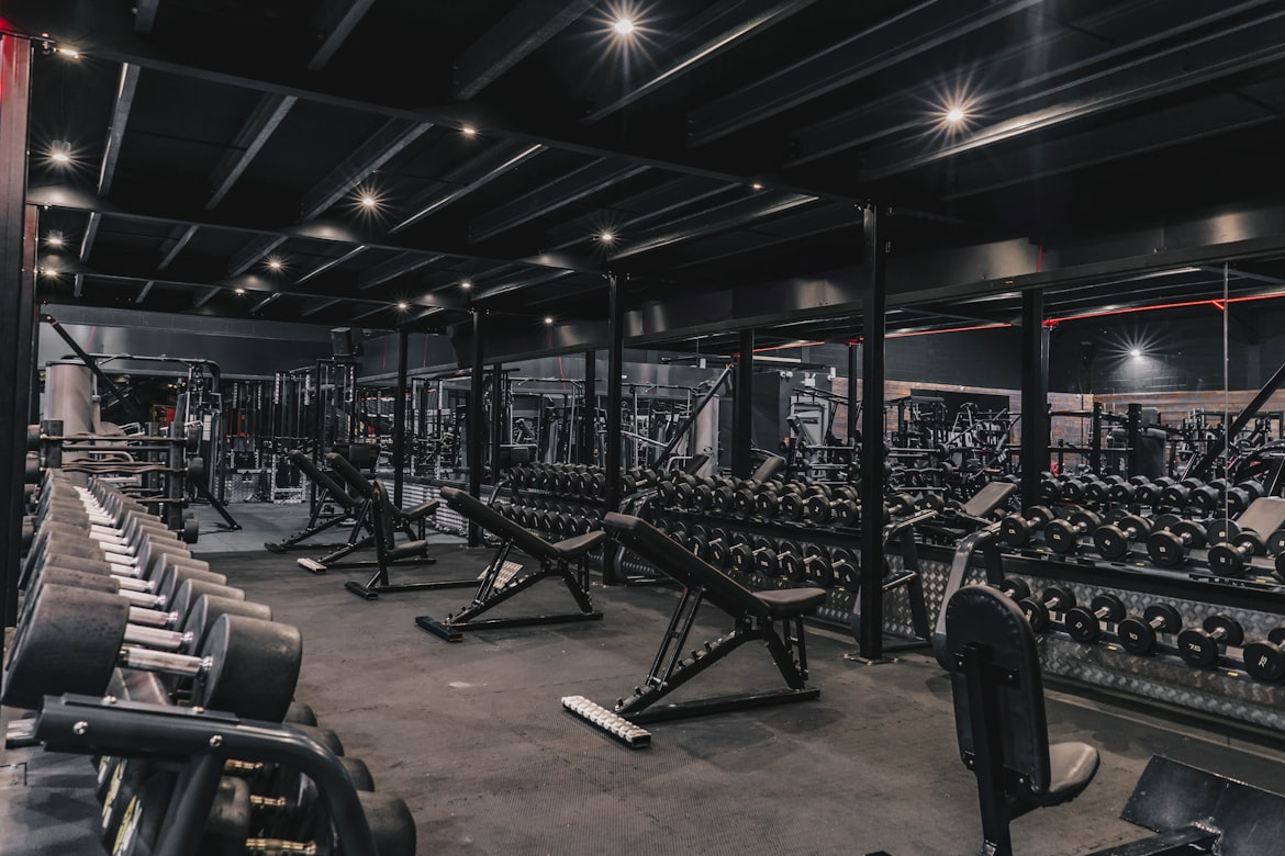 Dark modern gym interior with dumbbell racks, benches, and mirrors