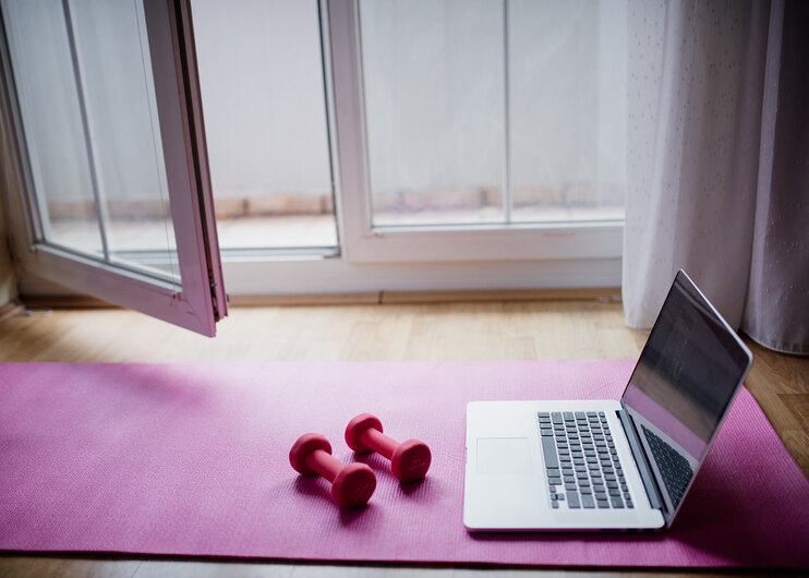 Laptop and small dumbbells on a workout mat for at-home training