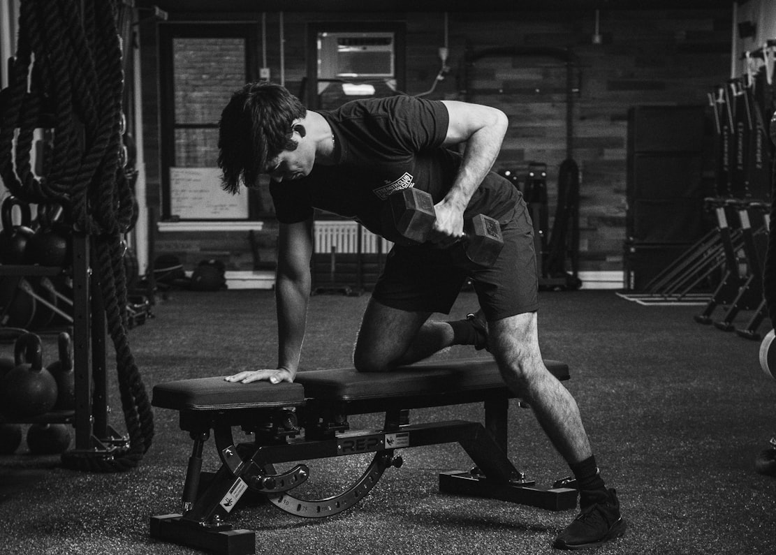 Man performing a one-arm dumbbell row on a bench in a dark gym