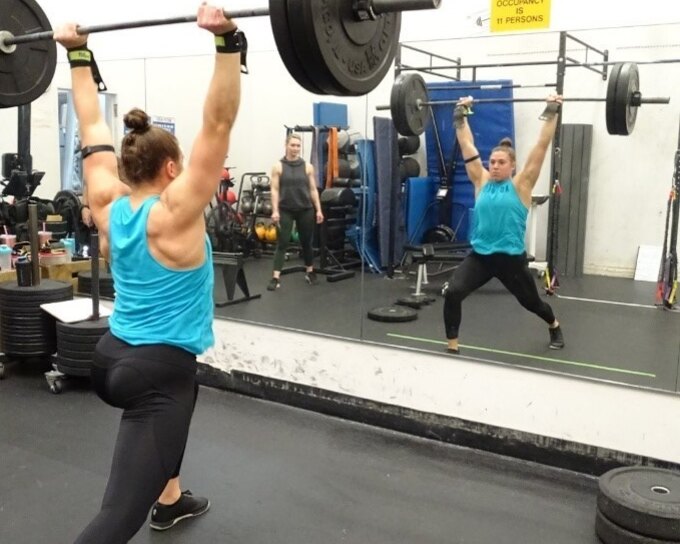 Female athlete lifting a barbell overhead in a functional fitness gym